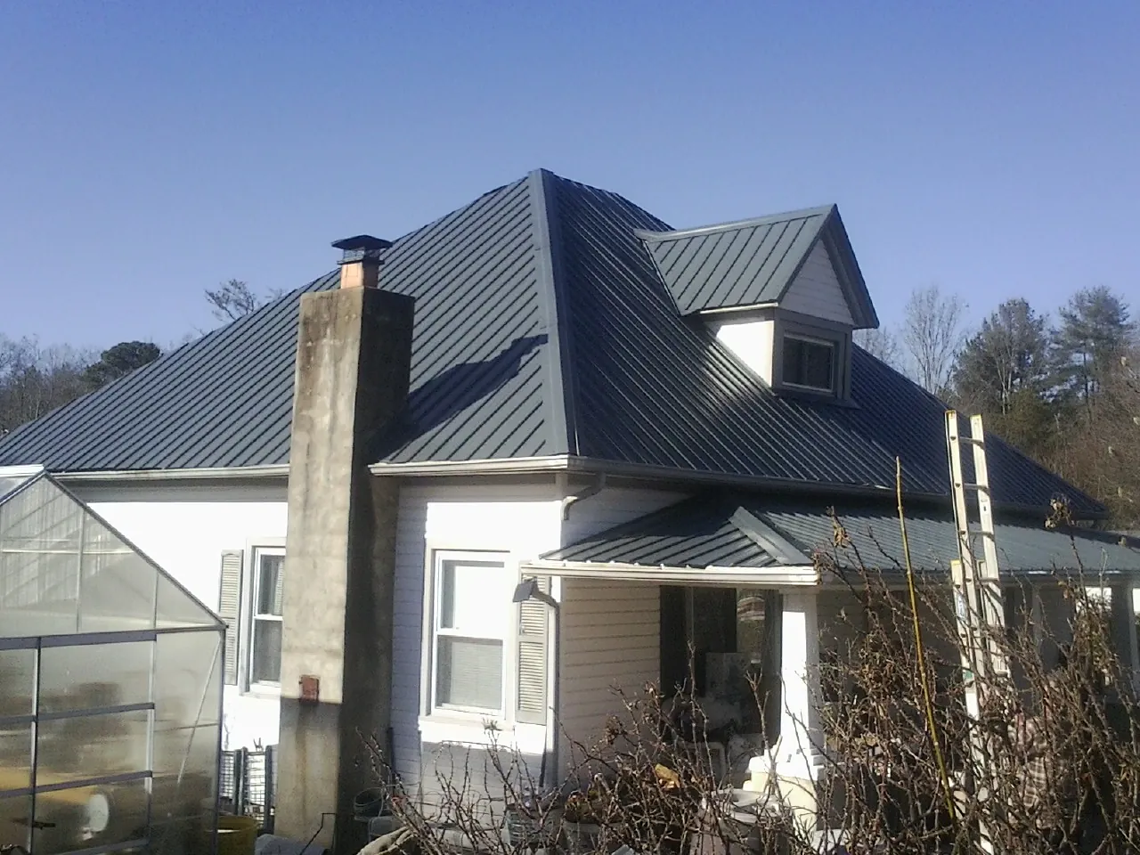 Dark blue standing seam metal roof on a white farmhouse with dormer — Slate & Tile Roof Repair by Roofing Brothers in Arnoldsburg