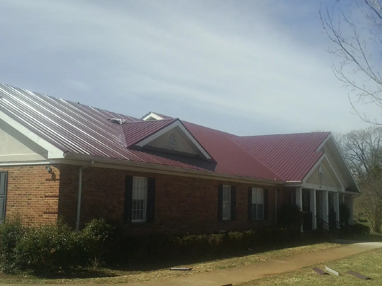 Red metal roof with gabled entries on a long brick building, from a Hail Damage Roof Repair job in Arnoldsburg