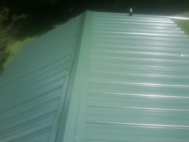 New green metal panels meeting at the ridge of a roof — Flat Roof Repair work by our crew in Arnoldsburg