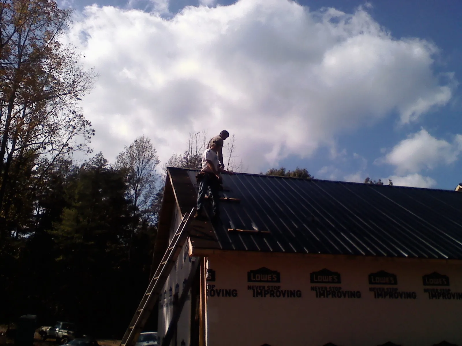 Roofer fastening dark metal panels high against a cloudy sky, from a Roof Inspection job in Arnoldsburg