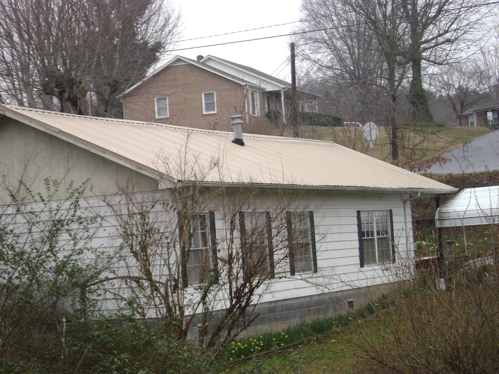 Tan metal roof on a white sided house set into a hillside — Commercial Roofing by Roofing Brothers in Arnoldsburg