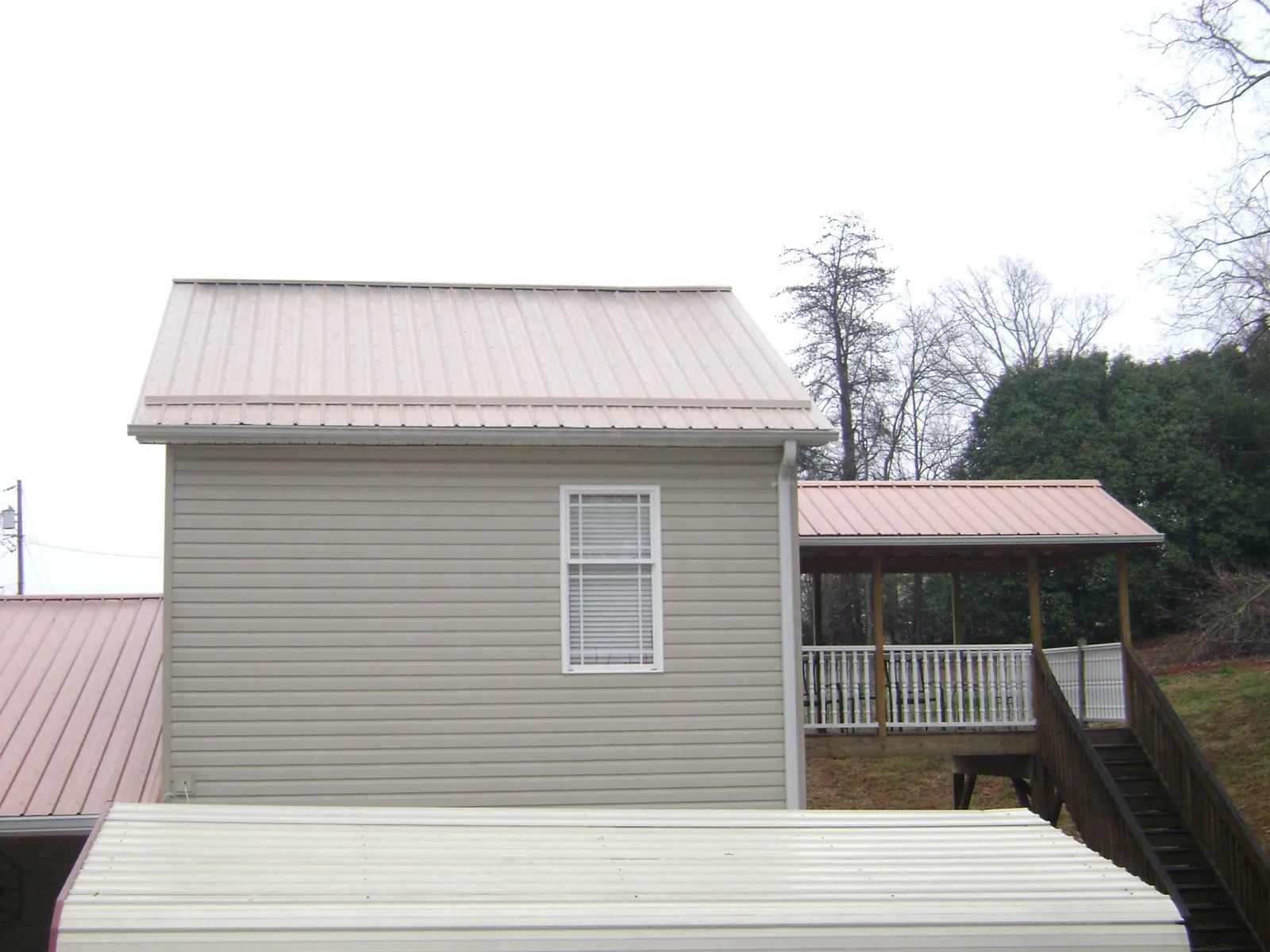 Tan metal roofs on a two story addition and attached porch, from a Roof Replacement job in Arnoldsburg